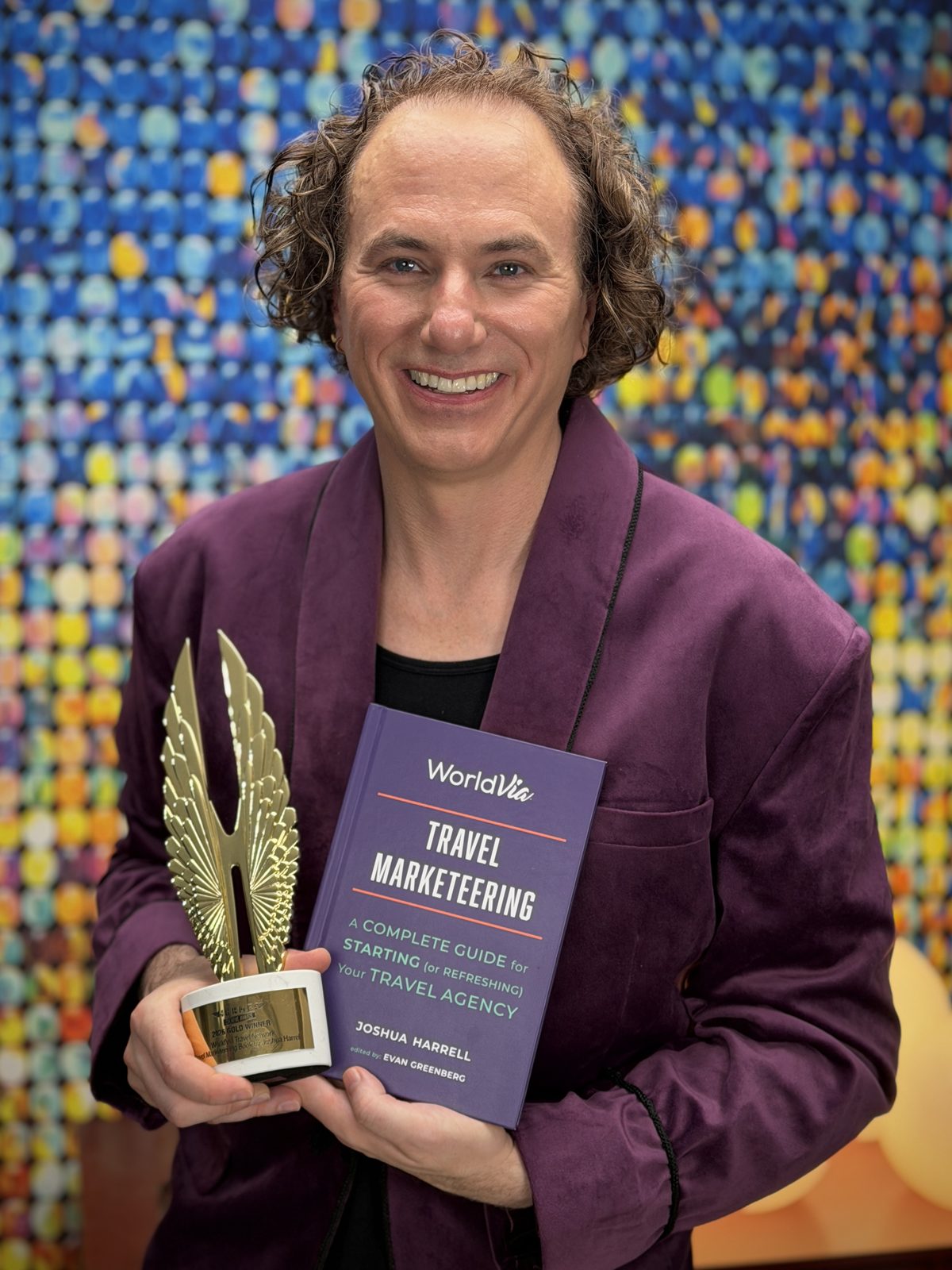Joshua Harrell holding his Gold 2026 Hermes Creative Award trophy and a copy of Travel Marketeering